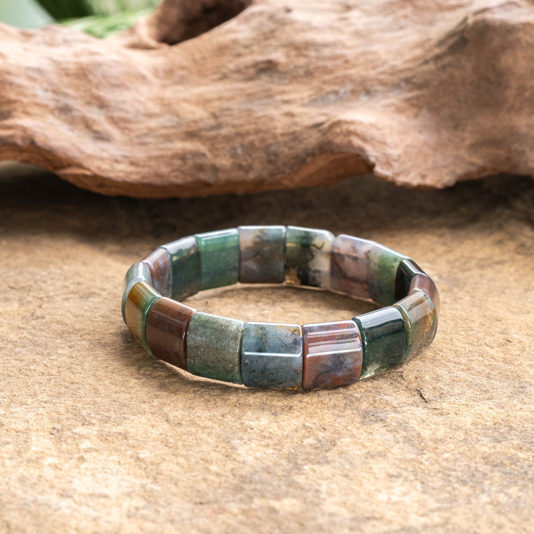 Wide agate gemstone bracelet on natural surface, showcasing unique colors.