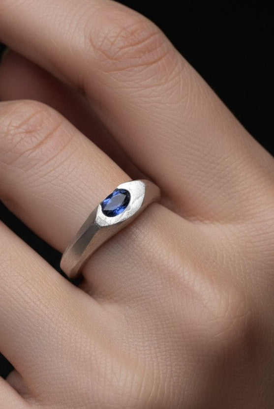 Silver ring with a blue gemstone on a hand against a black background