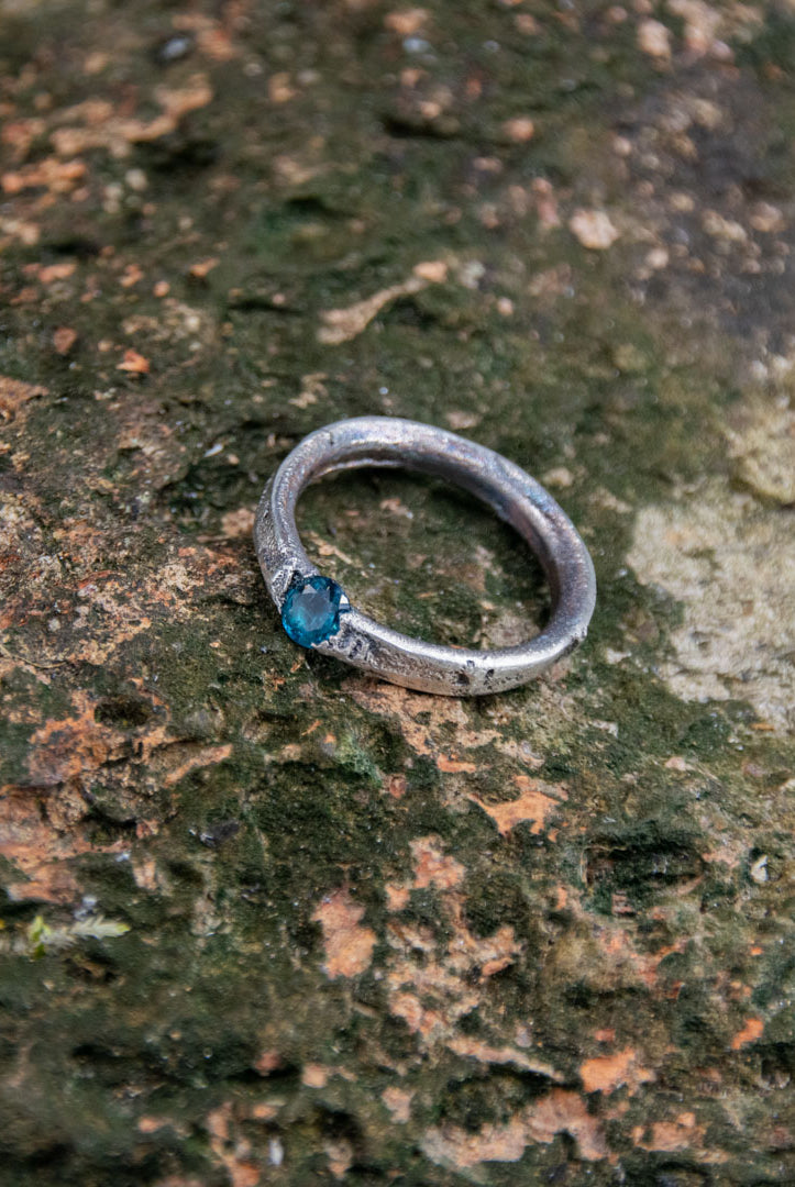 Handcrafted blue zirconia sandcasting ring on textured stone background, showcasing artisanal design.