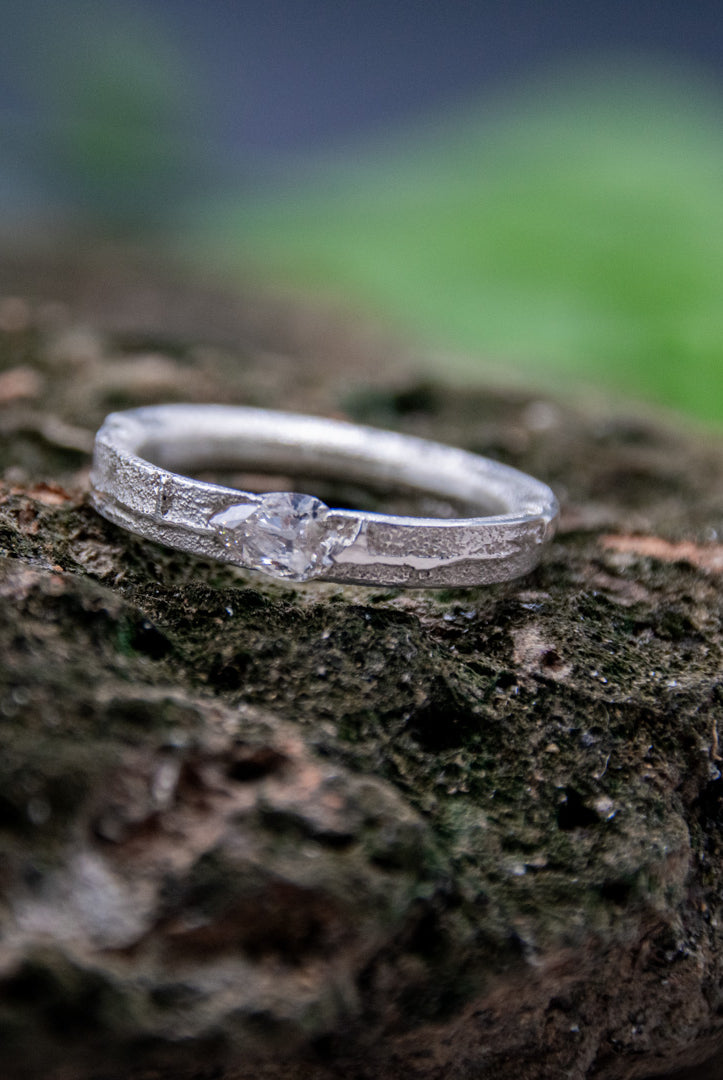 Crystal zirconia sandcasting ring with organic textures displayed on a natural rocky surface.