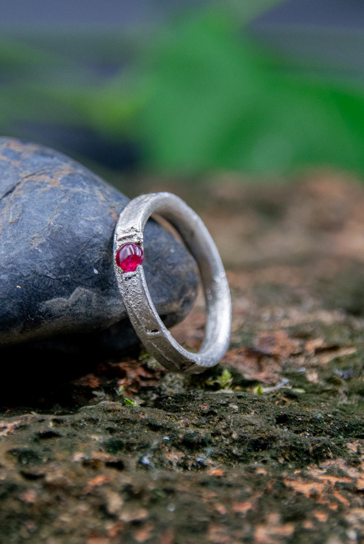 Round ruby sand casting ring on a textured rock surface, showcasing unique artisanal craftsmanship.