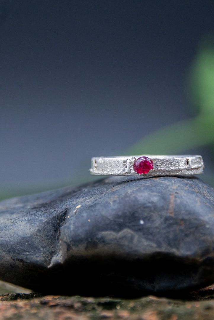 Unique round ruby sand casting ring on a textured stone surface, showcasing artisanal craftsmanship and organic designs.