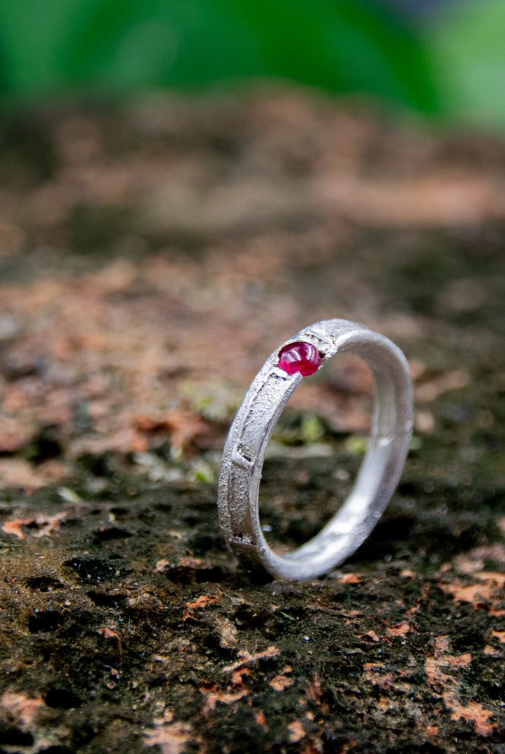 Round ruby sand casting ring showcasing organic textures and unique craftsmanship against a natural backdrop.