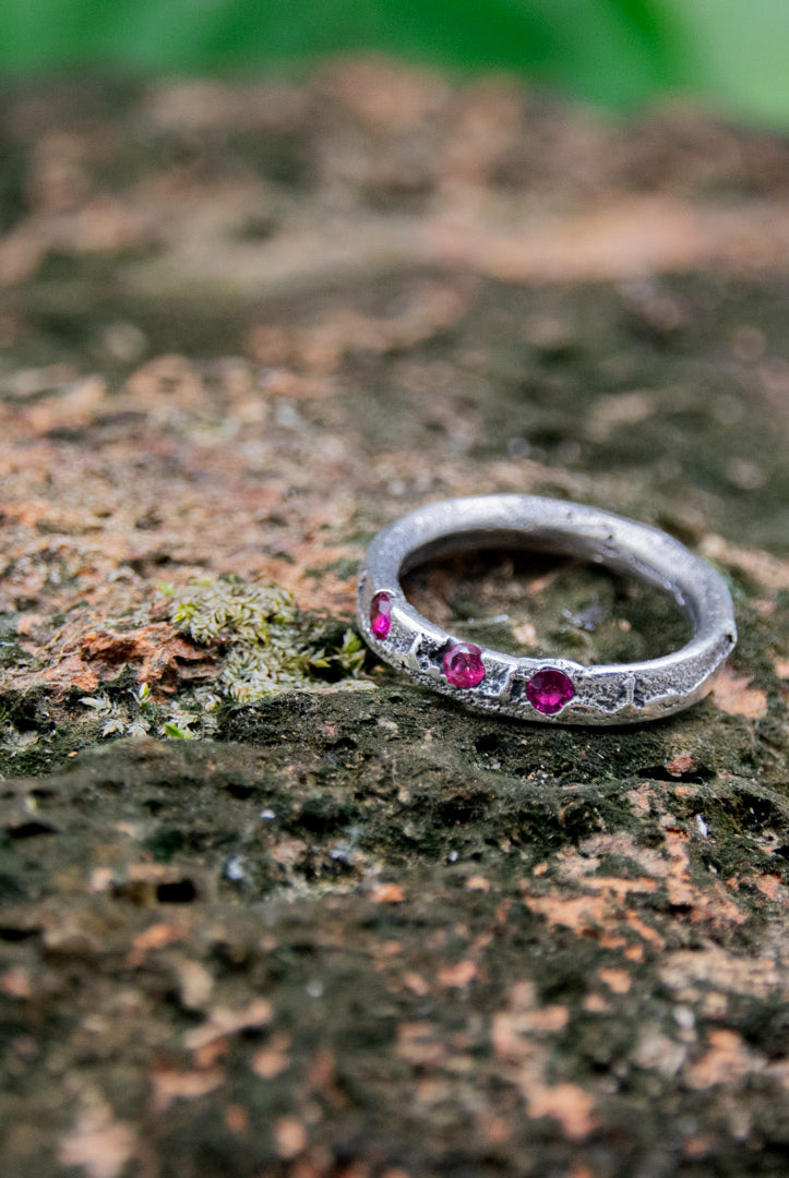 Three Little Ruby Sand Casting Ring featuring organic textures and unique design on a natural stone background.