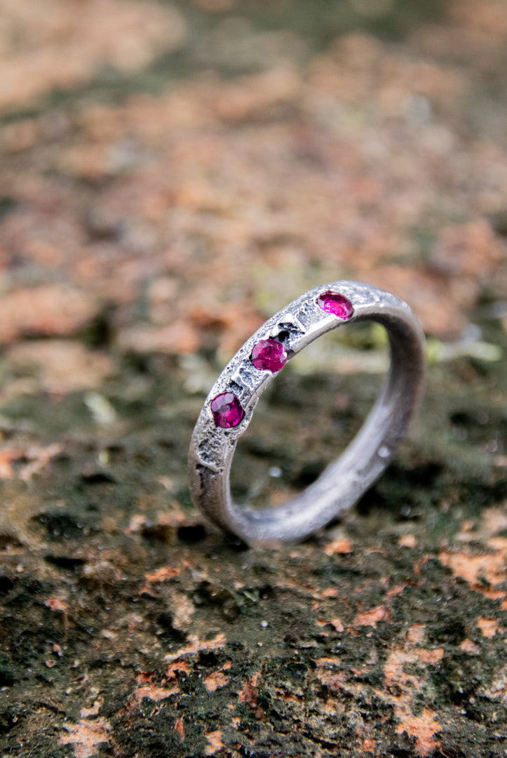 Three Little Ruby Sand Casting Ring featuring unique textures and three vibrant rubies on a rustic background.
