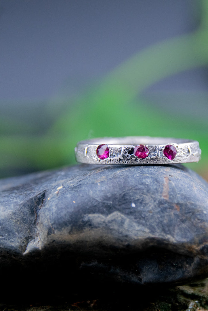 Three Little Ruby Sand Casting Ring on a smooth stone, showcasing unique artisanal craftsmanship and organic textures.