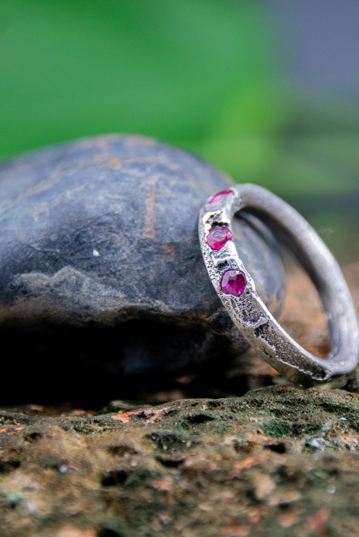 Three Little Ruby Sand Casting Ring showcasing unique textures and rubies set on a rock surface.