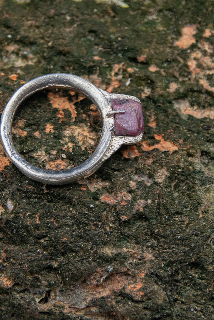 Raw ruby ring in sand casting style, showcasing unique textures on a natural stone background.