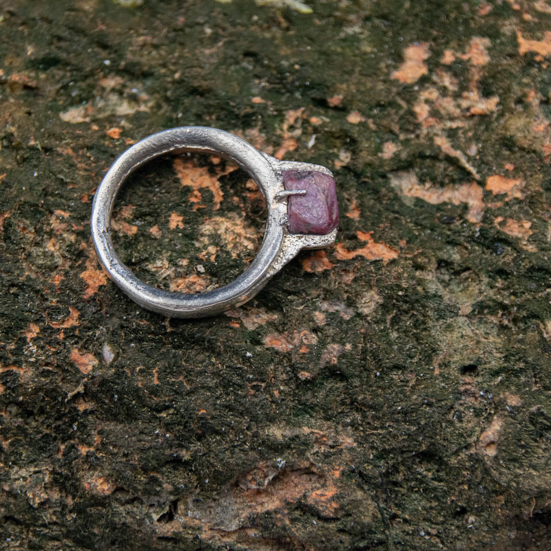 Raw ruby ring in sand casting style, showcasing unique textures on a natural stone background.