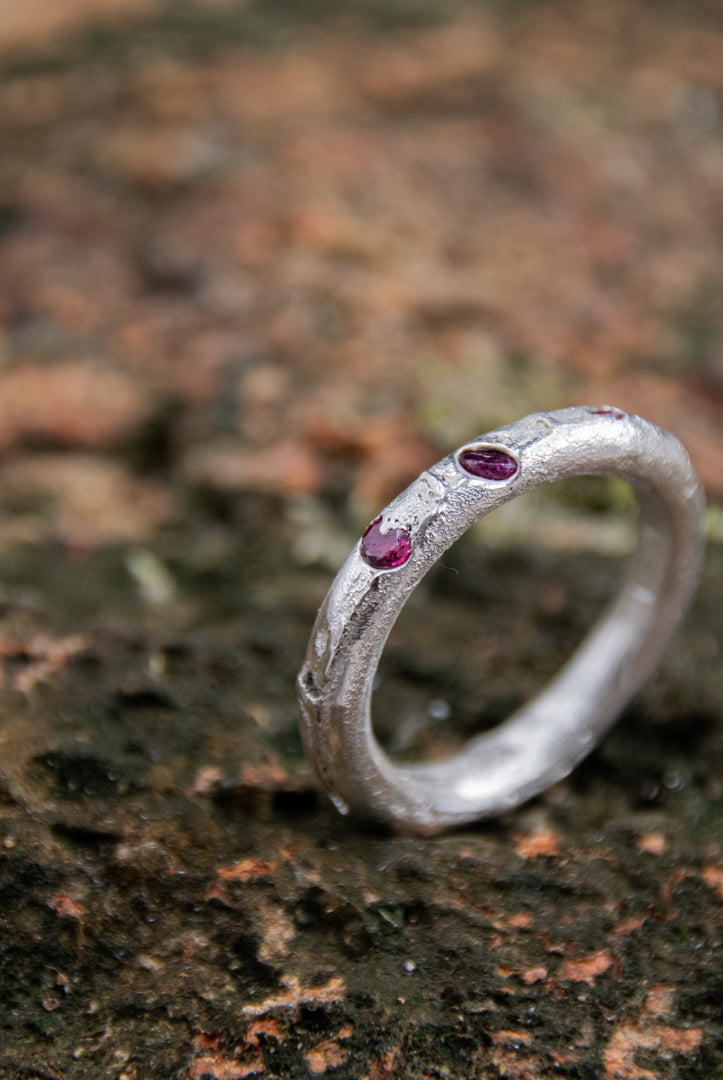 Round sandcast ring with three little rubies showcasing unique organic textures.