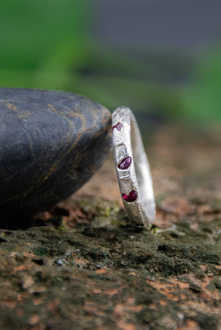 Three Little Ruby round sandcasting ring showcasing unique textures and garnet stones on a natural stone background.