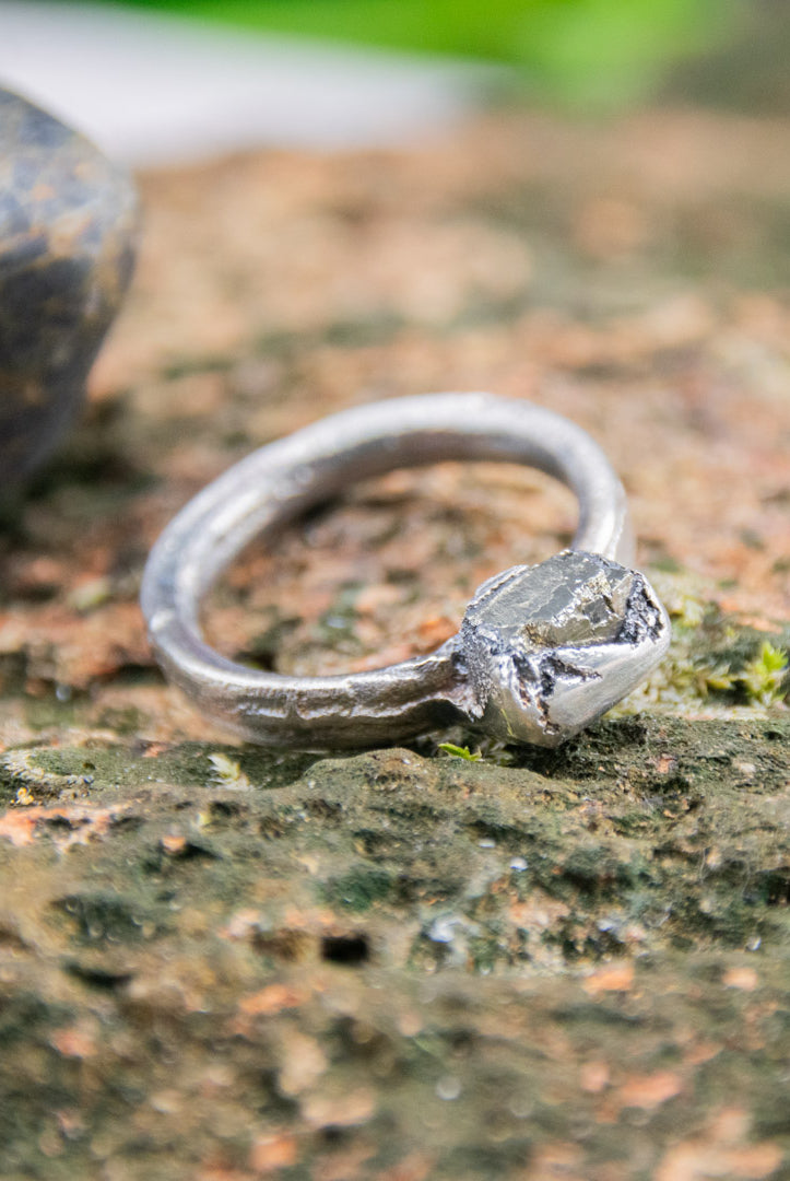 Handcrafted pyrite gemstone ring featuring unique sandcast design on natural stone surface.