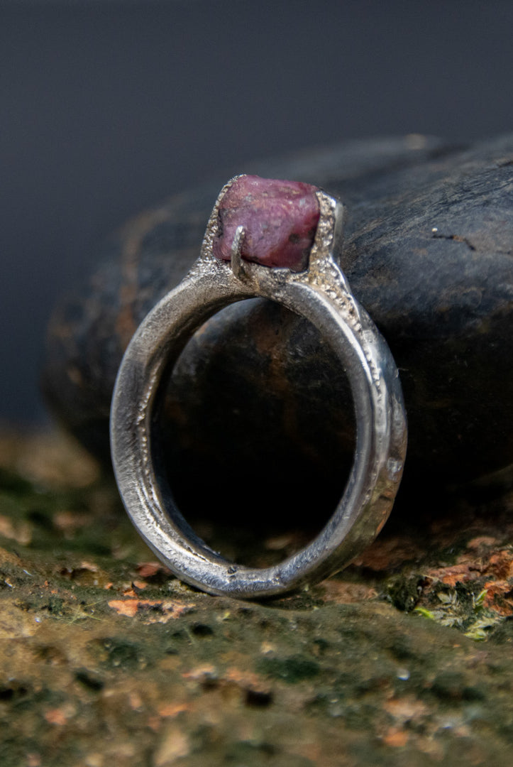 Raw ruby ring with organic textures, crafted using sandcasting technique, placed on a natural stone background.