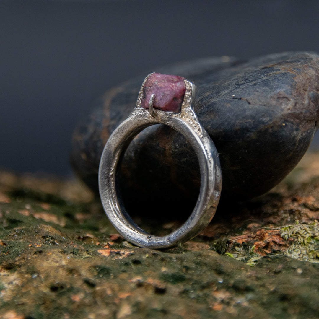 Raw ruby ring with organic textures, crafted using sandcasting technique, placed on a natural stone background.