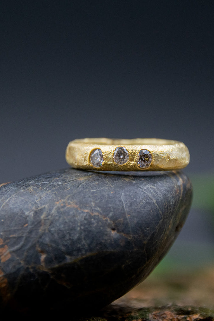 14K gold ring with moissanite gemstones, showcasing unique sandcasting texture and organic design, displayed on a stone.