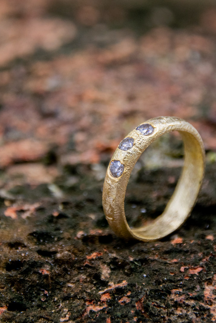 14K gold sand-cast ring featuring three sparkling moissanite stones, showcasing unique artisanal craftsmanship.