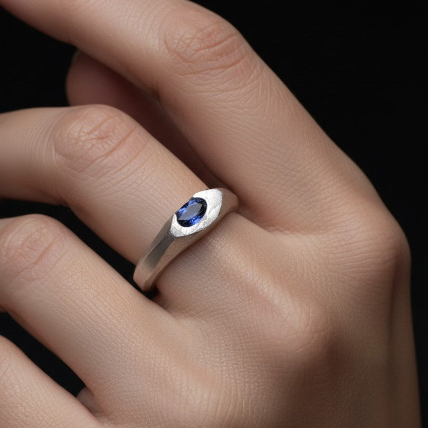 Silver ring with a blue gemstone on a hand against a black background