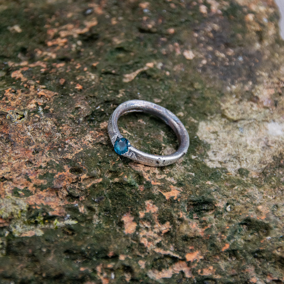 Handcrafted blue zirconia sandcasting ring on textured stone background, showcasing artisanal design.