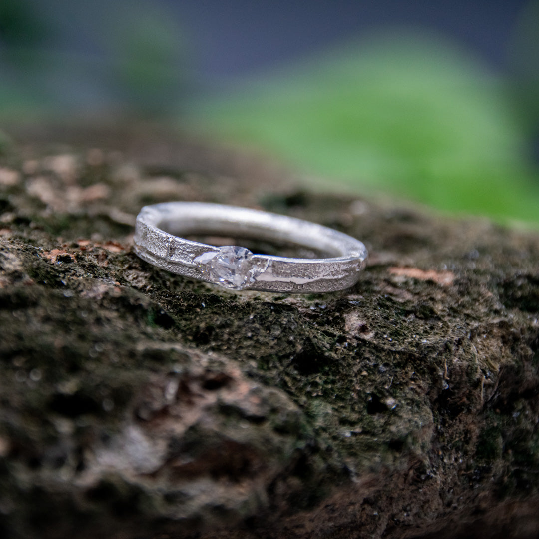 Crystal zirconia sandcasting ring with organic textures displayed on a natural rocky surface.