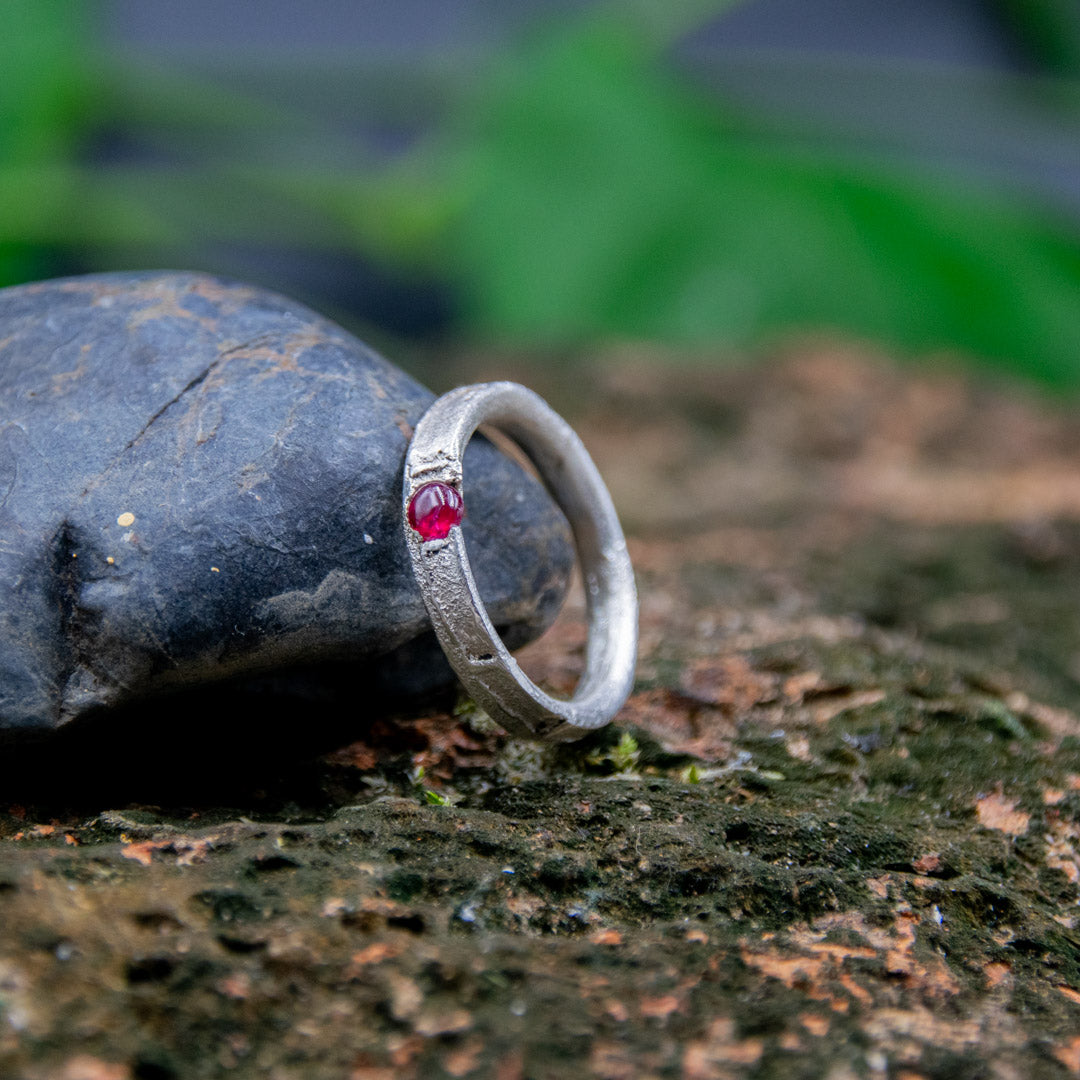 Round ruby sand casting ring on a textured rock surface, showcasing unique artisanal craftsmanship.