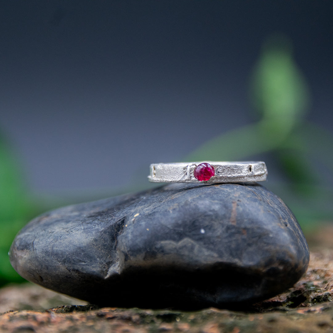 Unique round ruby sand casting ring on a textured stone surface, showcasing artisanal craftsmanship and organic designs.