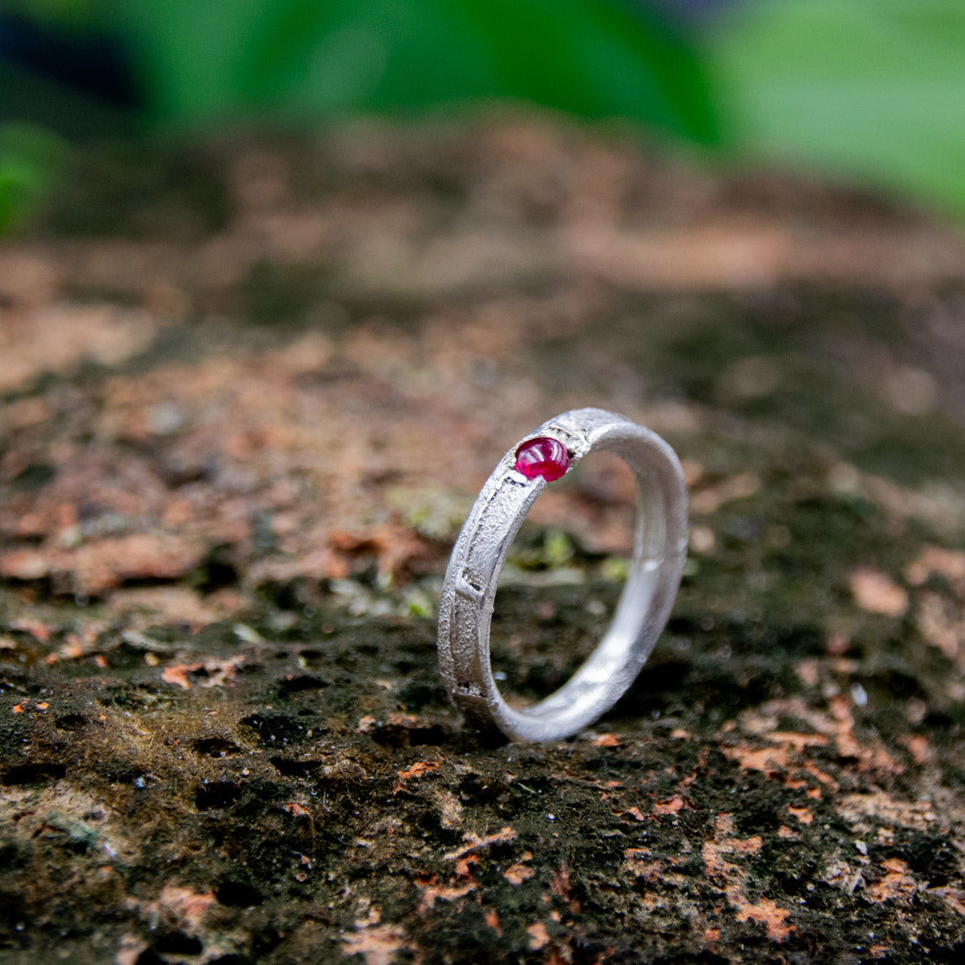 Round ruby sand casting ring showcasing organic textures and unique craftsmanship against a natural backdrop.