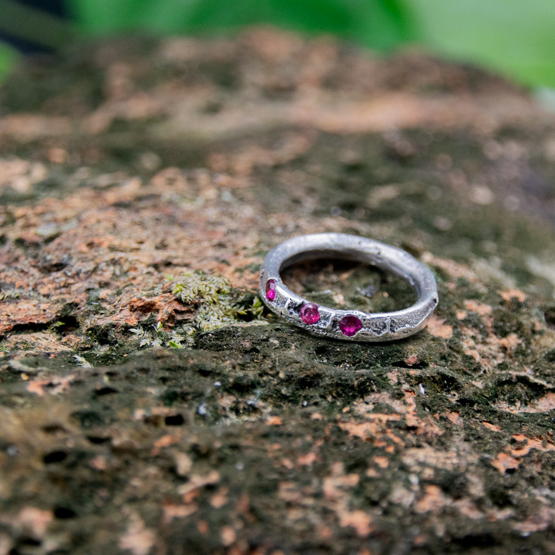 Three Little Ruby Sand Casting Ring featuring organic textures and unique design on a natural stone background.