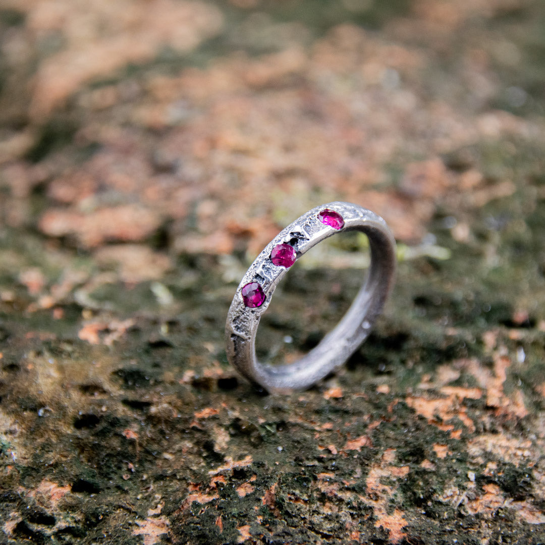 Three Little Ruby Sand Casting Ring featuring unique textures and three vibrant rubies on a rustic background.