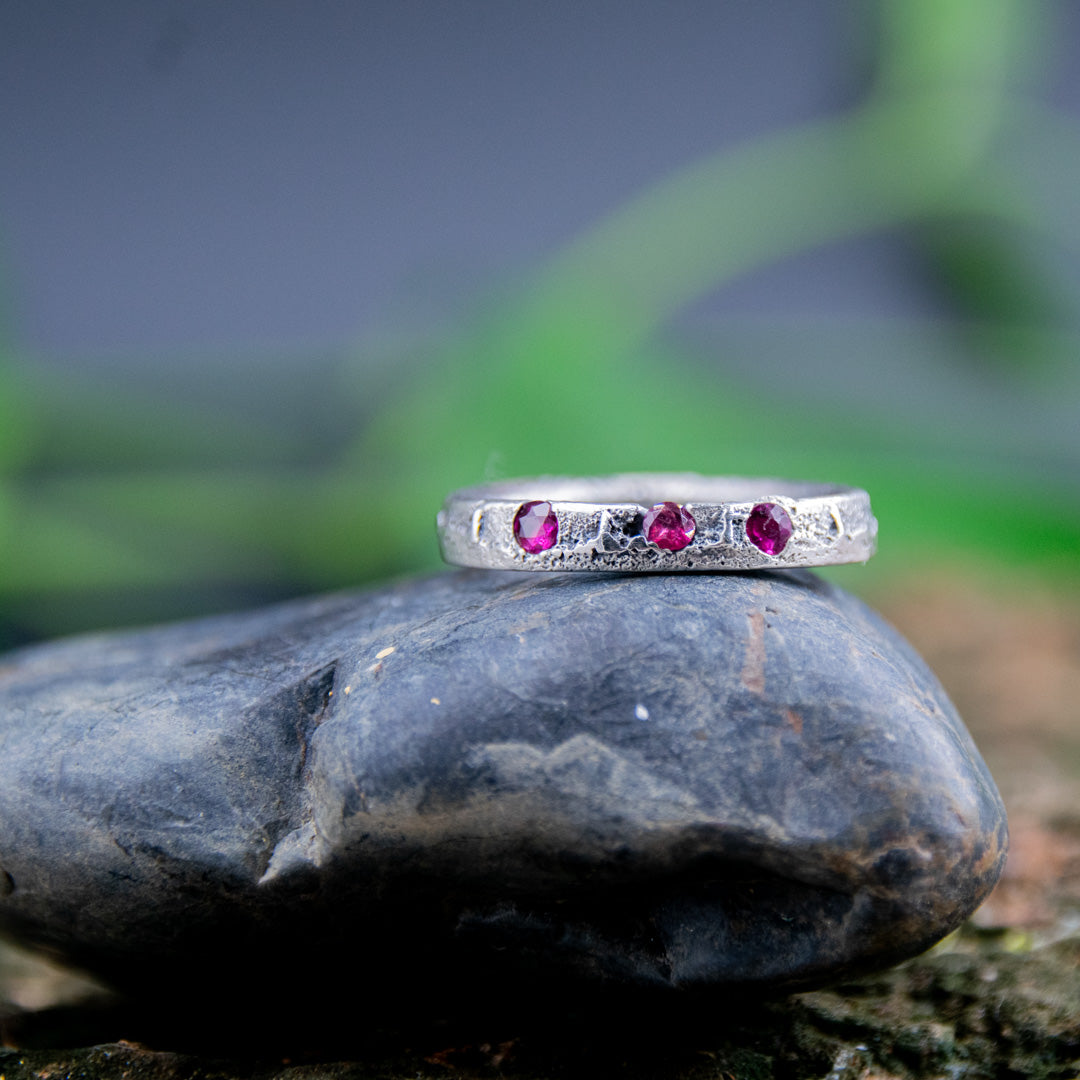Three Little Ruby Sand Casting Ring on a smooth stone, showcasing unique artisanal craftsmanship and organic textures.