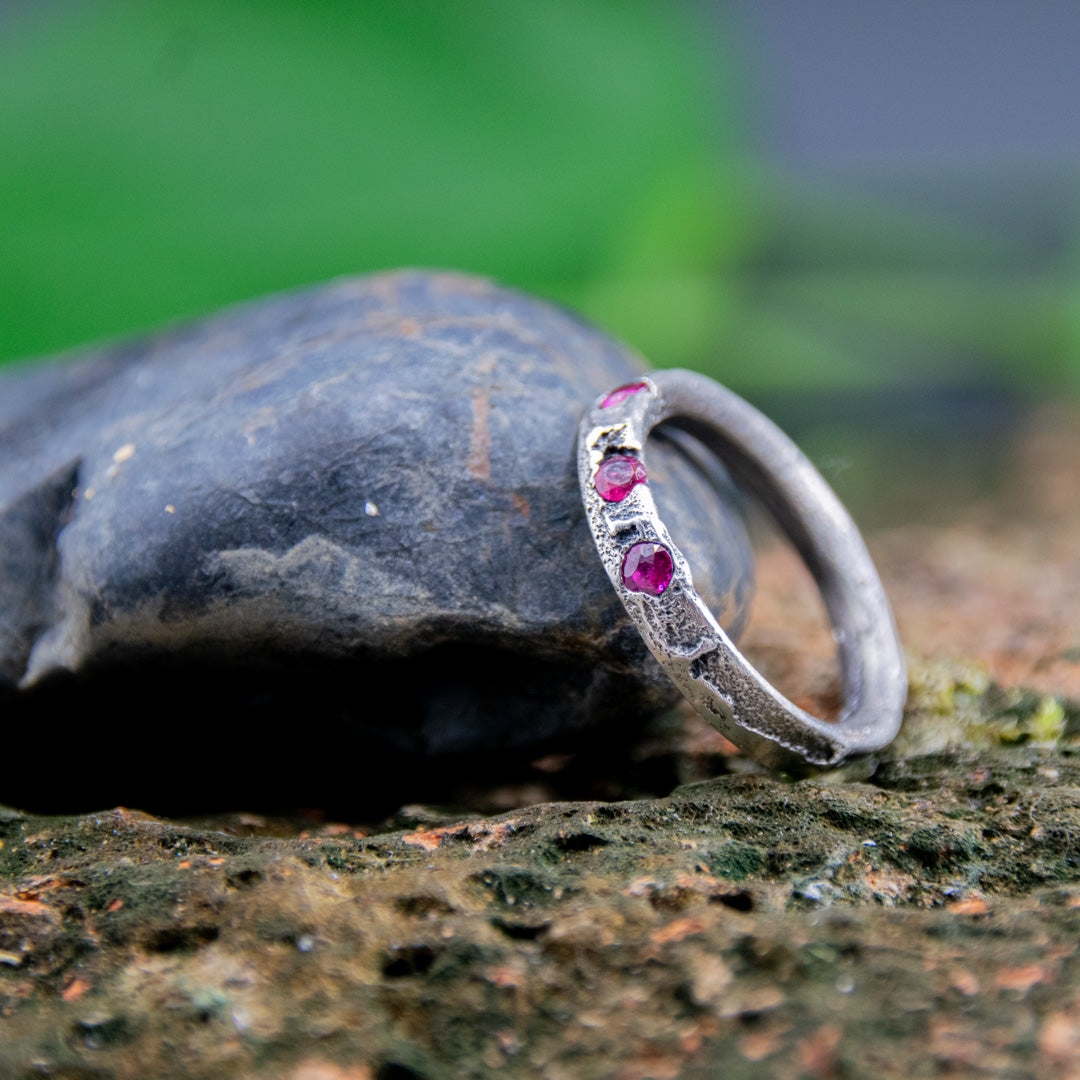 Three Little Ruby Sand Casting Ring showcasing unique textures and rubies set on a rock surface.