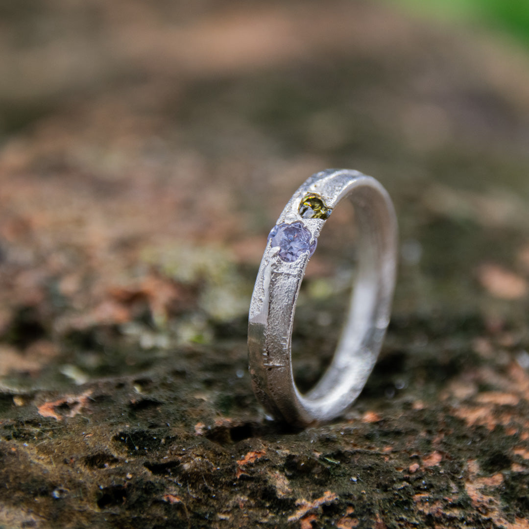 Close-up of a unique purple and brownish zirconia sand casting ring on textured surface.