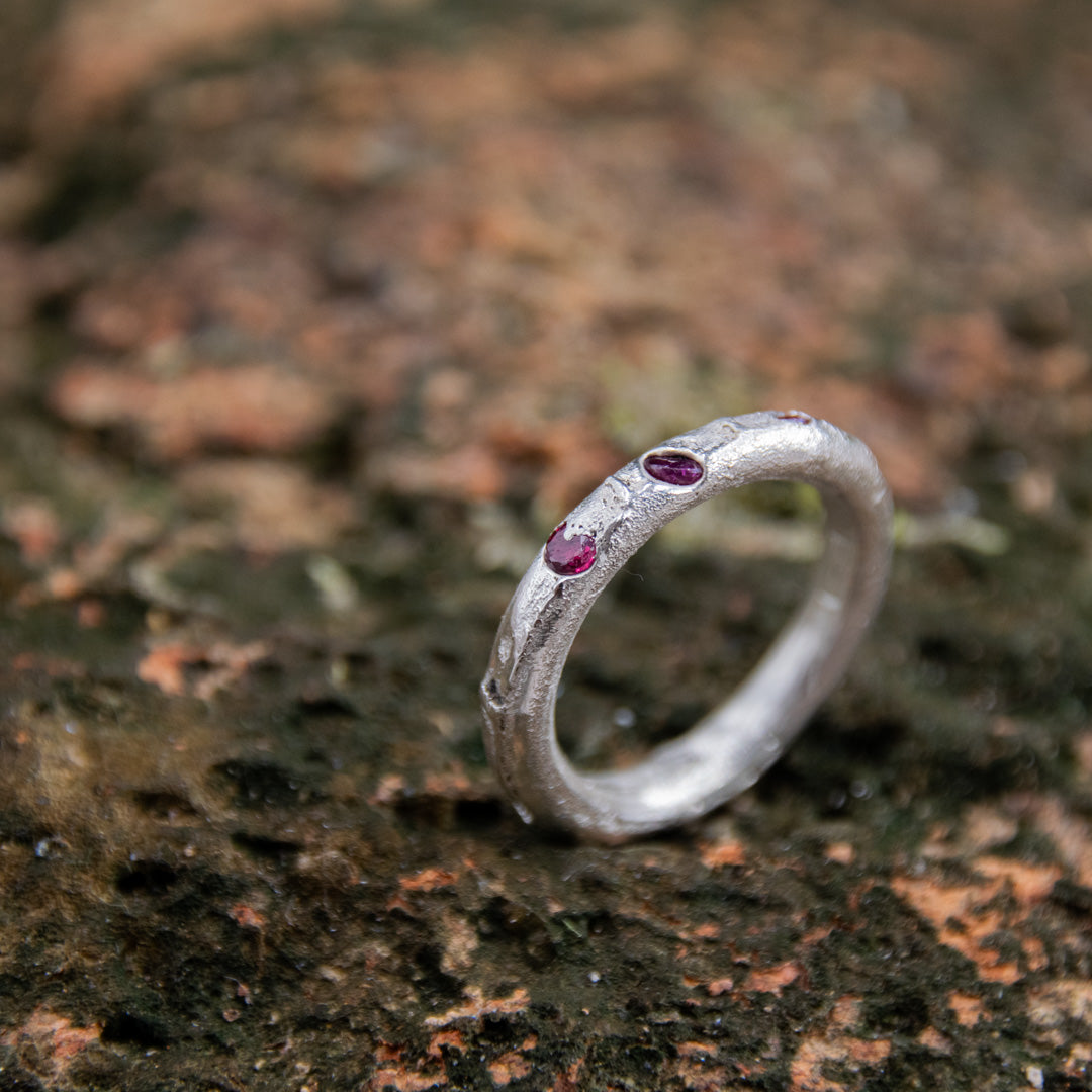 Round sandcast ring with three little rubies showcasing unique organic textures.