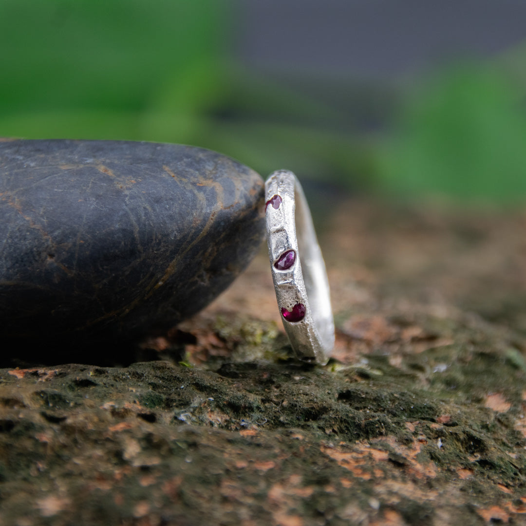Three Little Ruby round sandcasting ring showcasing unique textures and garnet stones on a natural stone background.