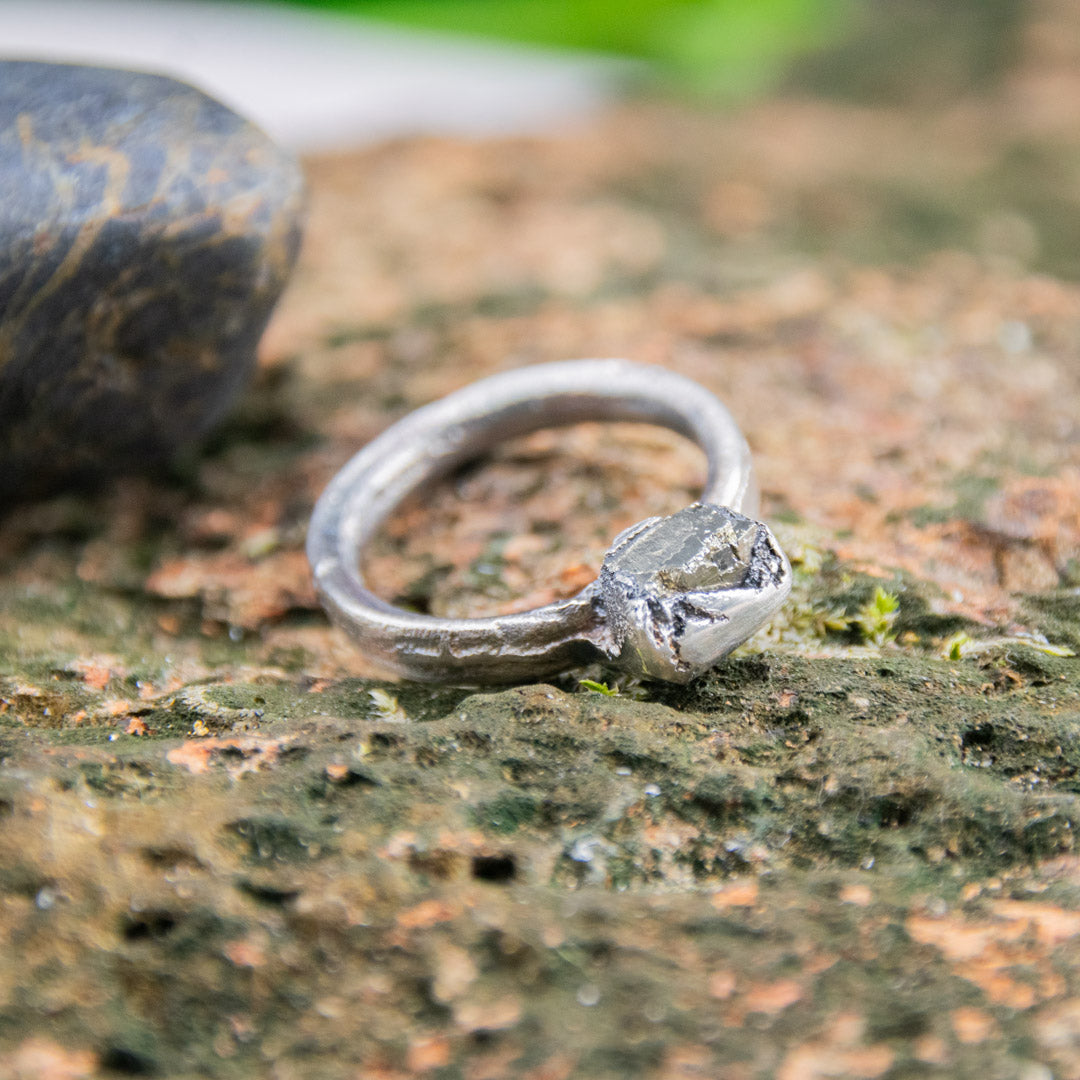 Handcrafted pyrite gemstone ring featuring unique sandcast design on natural stone surface.