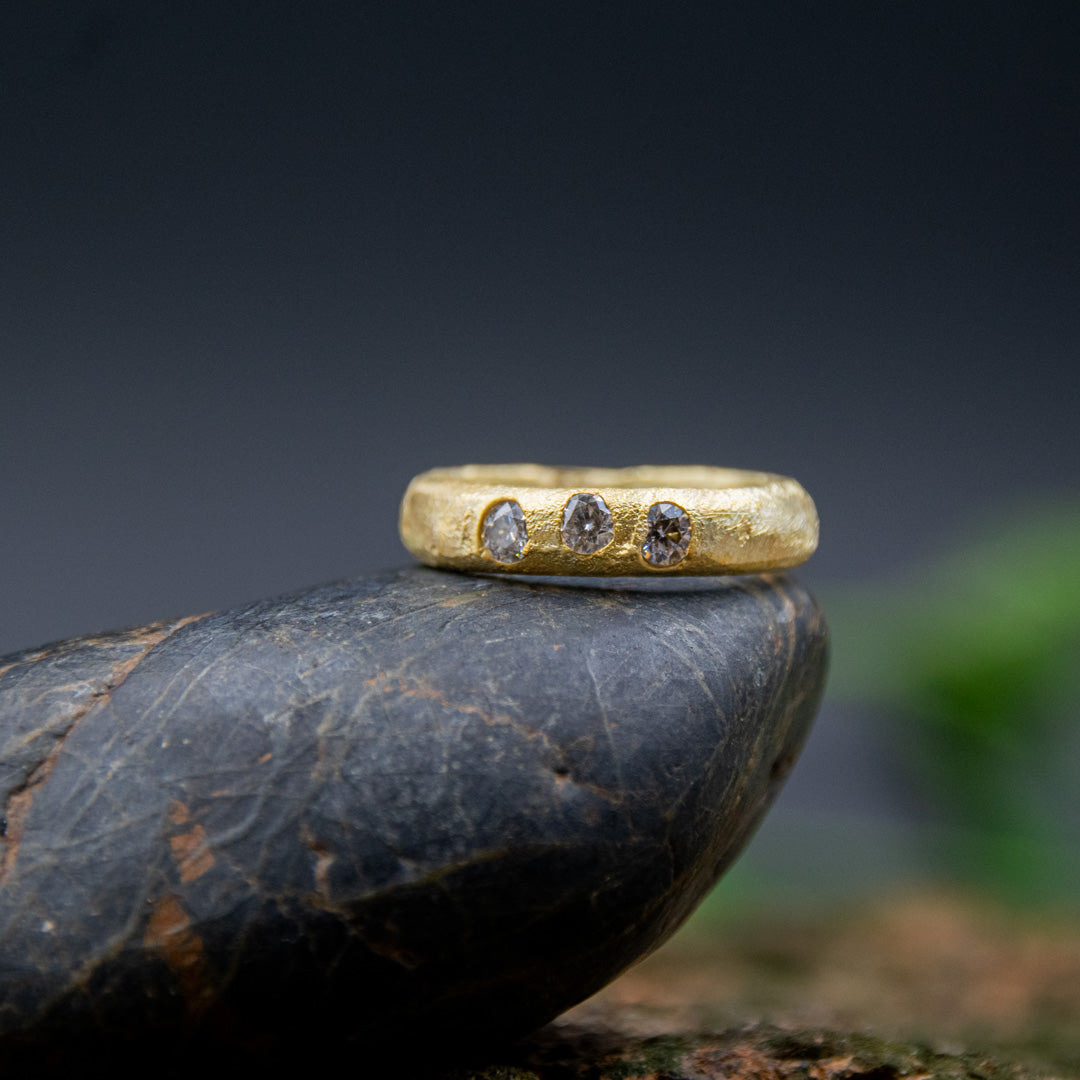 14K gold ring with moissanite gemstones, showcasing unique sandcasting texture and organic design, displayed on a stone.