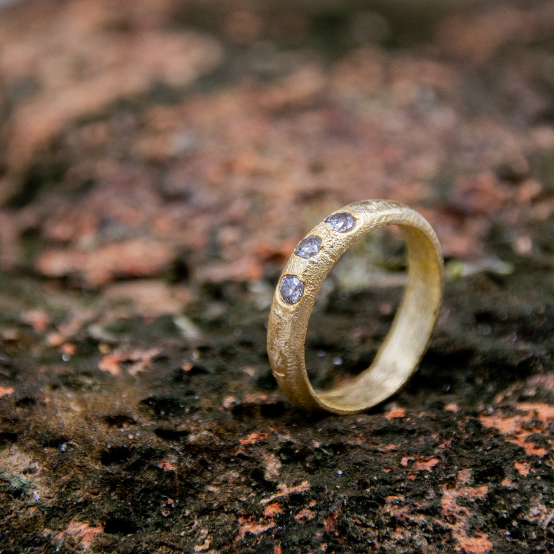 14K gold sand-cast ring featuring three sparkling moissanite stones, showcasing unique artisanal craftsmanship.