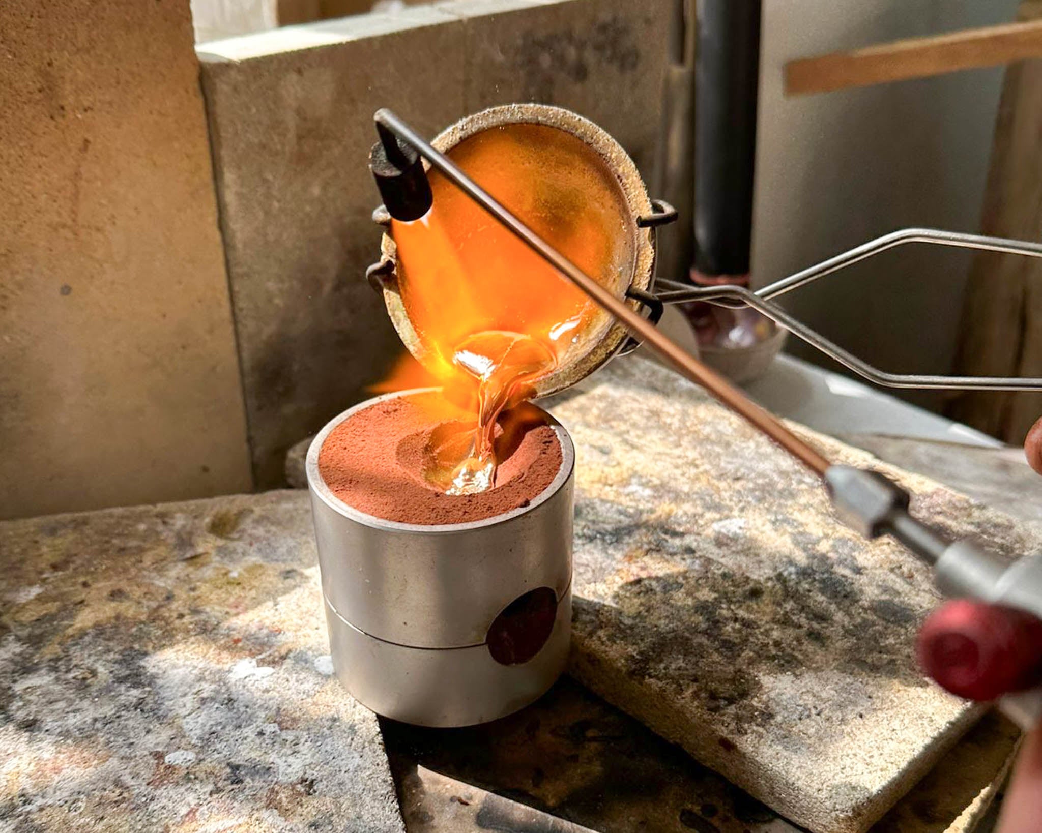 Pouring molten silver into sand mold in Koh Chang jewelry studio, goldsmith technique.